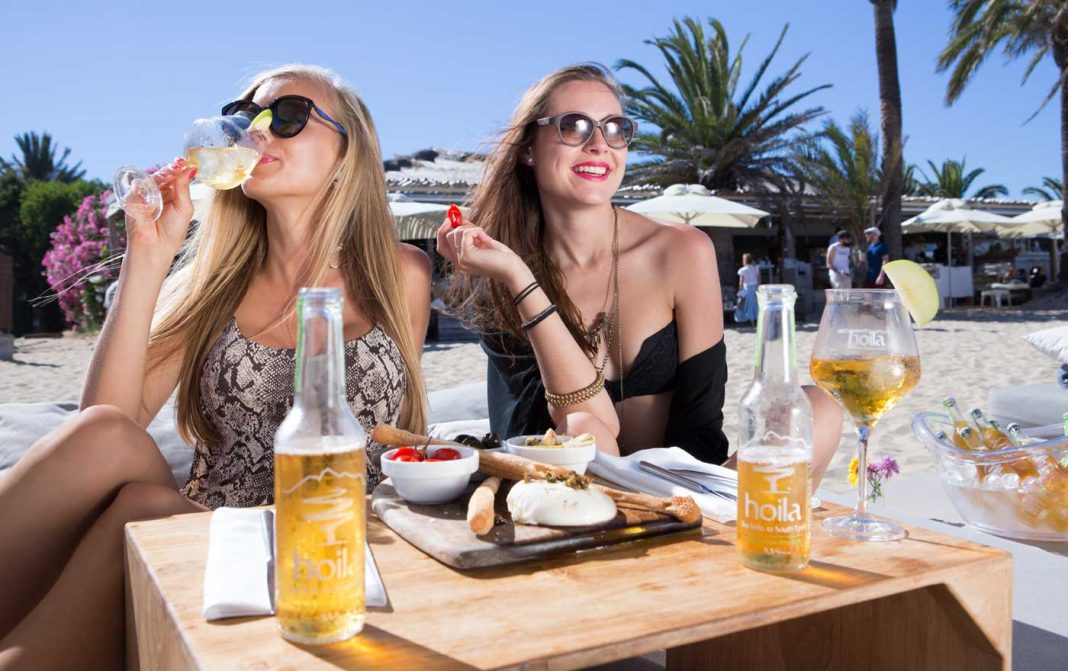 Dos jóvenes turistas disfrutando de una bebida en un ‘beach club’ sobre la fina arena de una playa. AISHA BONET